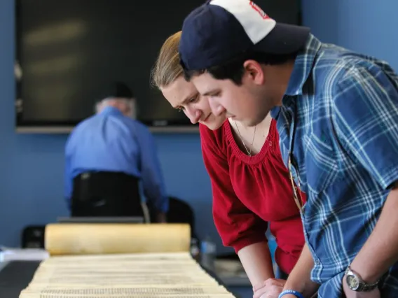 one man and one woman looking at the Torah